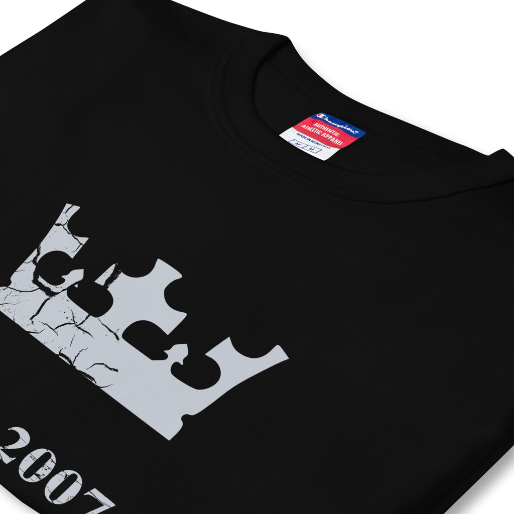 Folded side profile of black heavyweight, 100% cotton luxury Champion© t-shirt featuring aged crown emblem and text "EST. 2007" indicating the year the faction was first introduced to the brick universe. Item is a BRKDrip Heritage Collection luxury shirt with a vintage castle building block aesthetic.