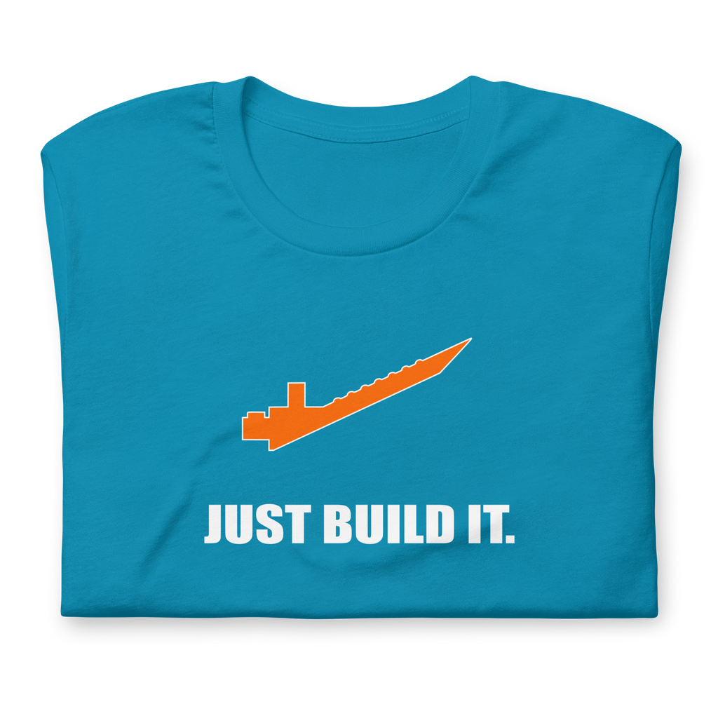 Folded aqua blue 100% airlume cotton t-shirt featuring orange brick separator and parody AFOL saying: "Just Build It". Item is a BRKDrip AFOL essentials shirt with a modern brick-inspired aesthetic.