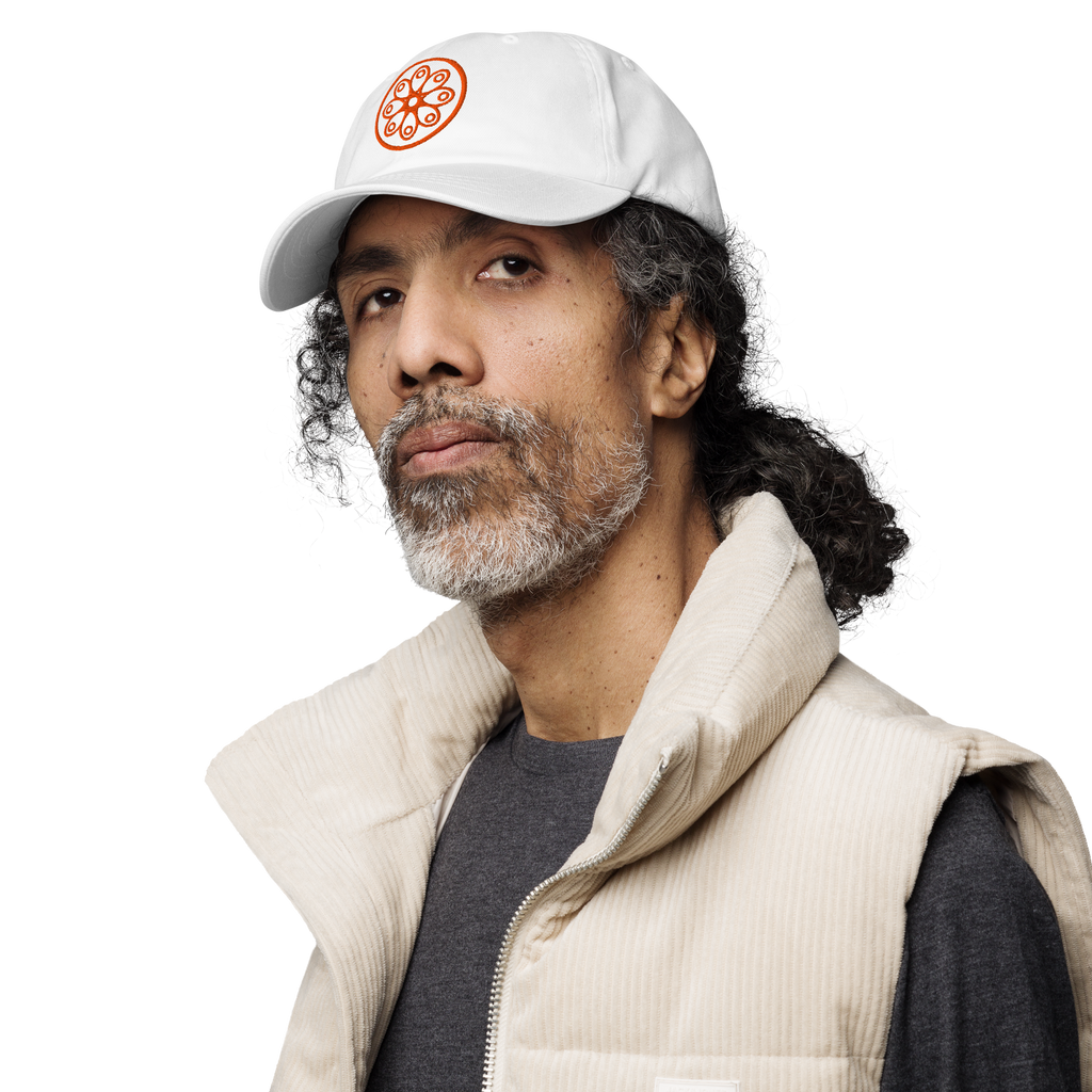 Fashionable male model wearing a white cotton twill baseball cap hat featuring embroidered orange sensei dojo logo design. Item is a BRKDrip AFOL Headgear Dad Hat with a modern elemental brick master aesthetic.