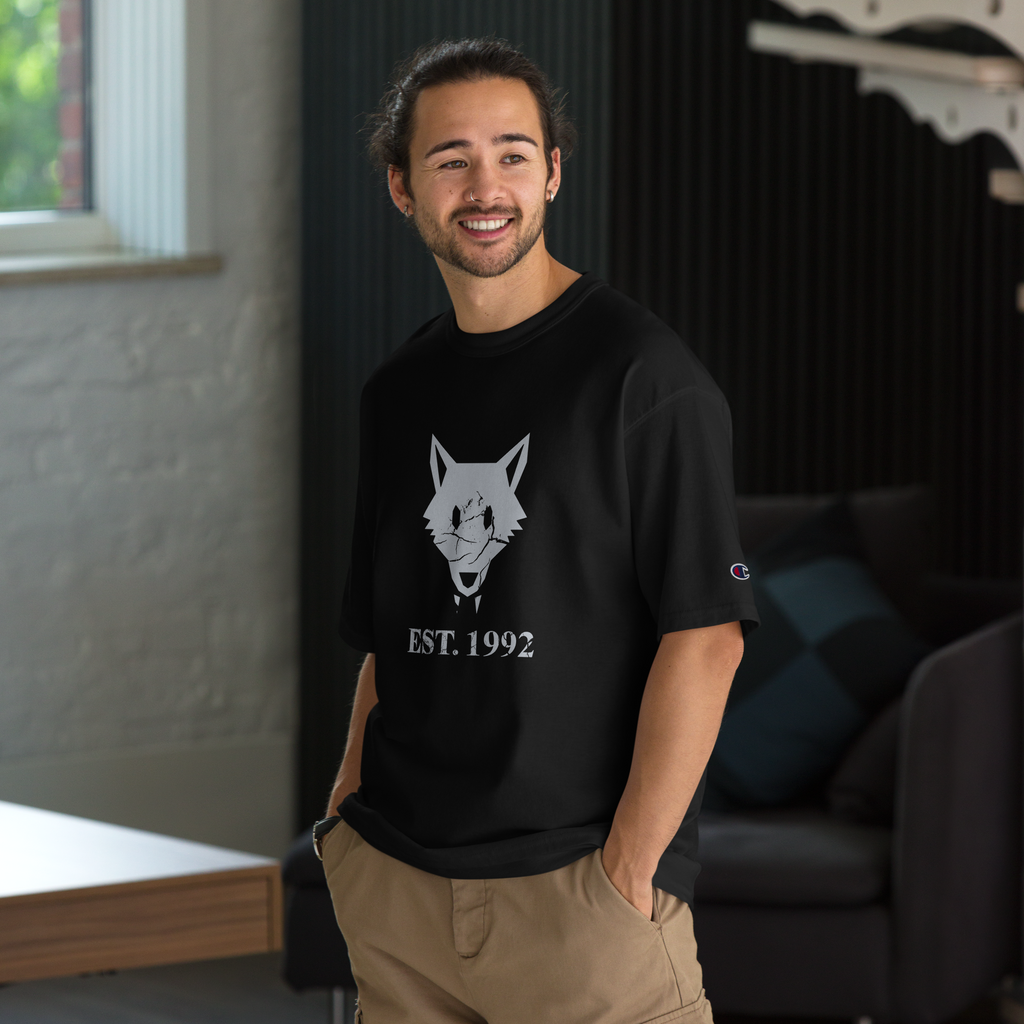Fashionable male model wearing oversized black heavyweight, 100% cotton luxury Champion© t-shirt featuring aged wolfpack emblem and text "EST. 1992" indicating the year the faction was first introduced to the brick universe. Item is a BRKDrip Heritage Collection luxury shirt with a vintage castle building block aesthetic.